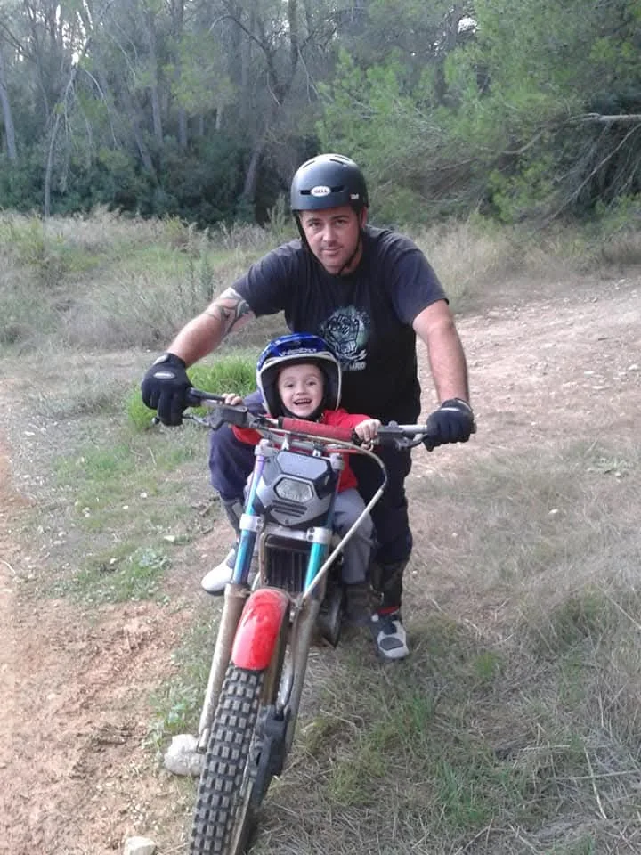 Adulto acompañando a un niño en una moto sobre tierra